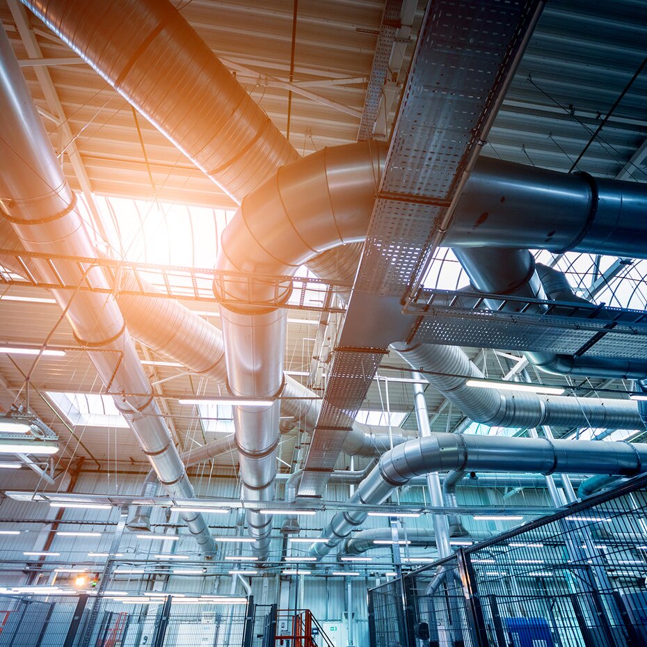 Lüftungsrohre in der Höhe eines großen grauen industriellen Raumes