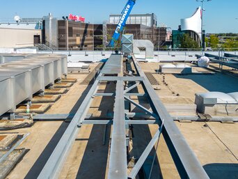 Große Stahlträger auf einem flachen Dach, im Hintergrund ein blauer mobiler Kran bei klarem Himmel.