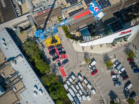 Luftaufnahme eines urbanen Industriegebiets mit mehreren geparkten Autos und einem großflächigen Gebäude, das teilweise mit RLT-Anlagen bedeckt ist. Ein großer Kran erstreckt sich über das Dach.
